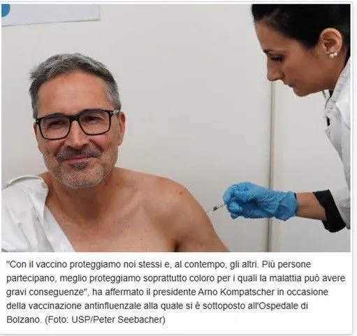 Un uomo riceve un’iniezione al braccio da un’operatrice sanitaria con guanti blu, in un ambulatorio medico.